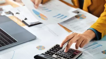 Person using a calculator with financial documents spread on the desk.