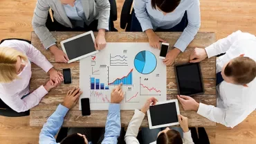 People collaborating over charts and tablets at a table.