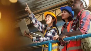 Group of workers in safety gear looking up, one holding a laptop.