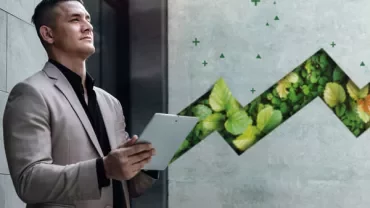 Person in a suit holding a tablet, standing next to a green leafy graphic on a wall.