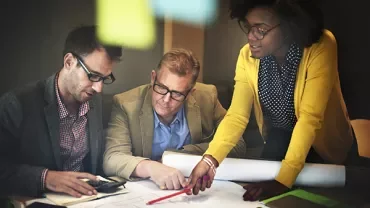Three people collaborating and discussing a project over architectural plans.