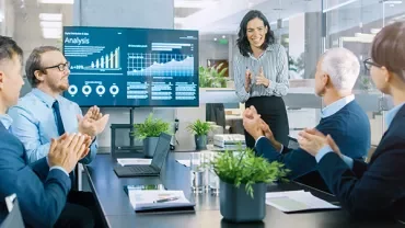 Team applauding a presentation with data charts on a screen.