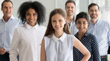 Group of six people smiling in an office setting.