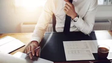 Person working at a desk with a laptop, documents, and a cup of coffee.