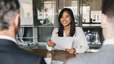 Person smiling and holding papers in a meeting room.