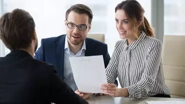 Two people conducting an interview, holding a resume, seated at a table.