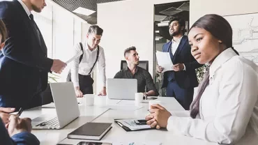 Group of people having a meeting in a modern office with laptops and paperwork.